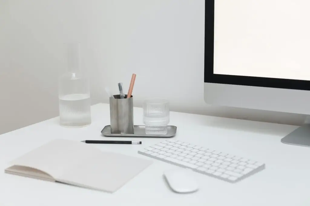 White desk with monitor, keyboard, mouse and open notebook
